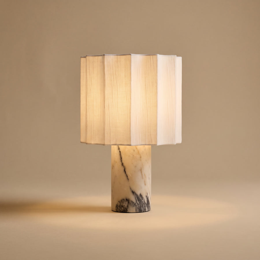 Macara marble and fabric table lamp, lit, on sand backdrop