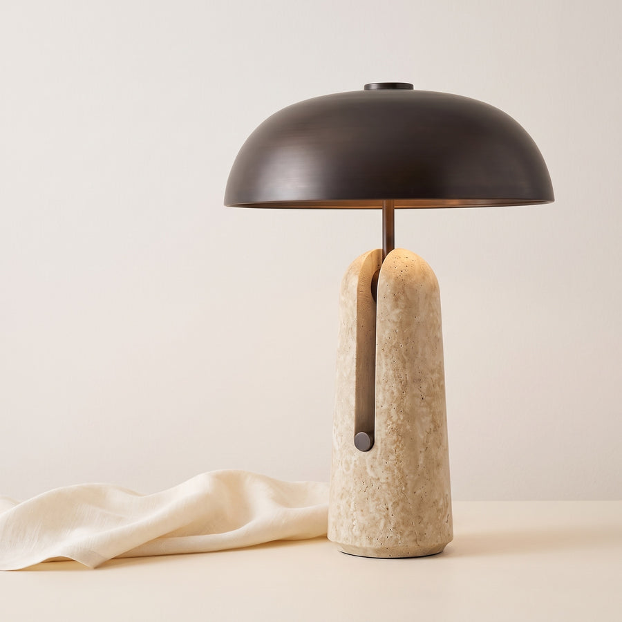 Sillon travertine and iron table lamp beside draped linen on off-white backdrop