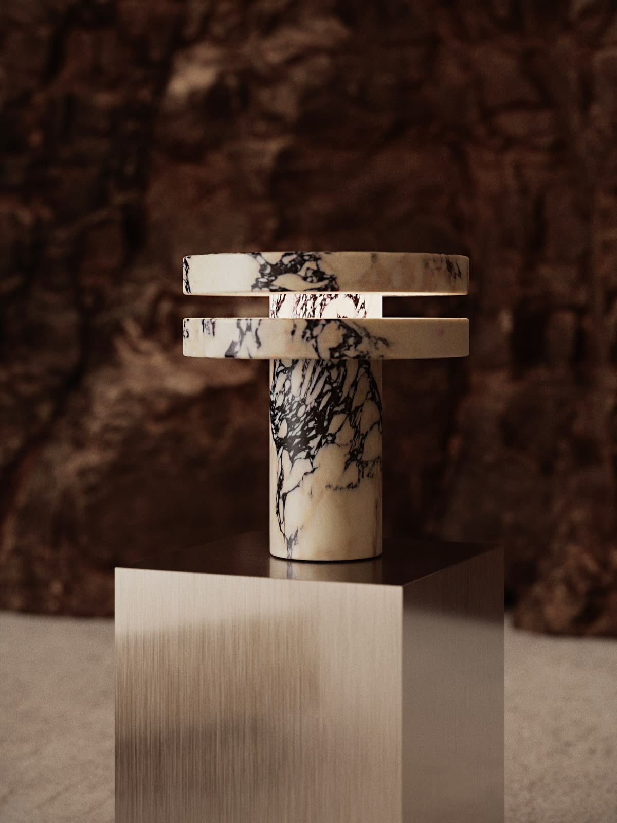 Strates marble table lamp, lit, on a brushed metal plinth before dark rock