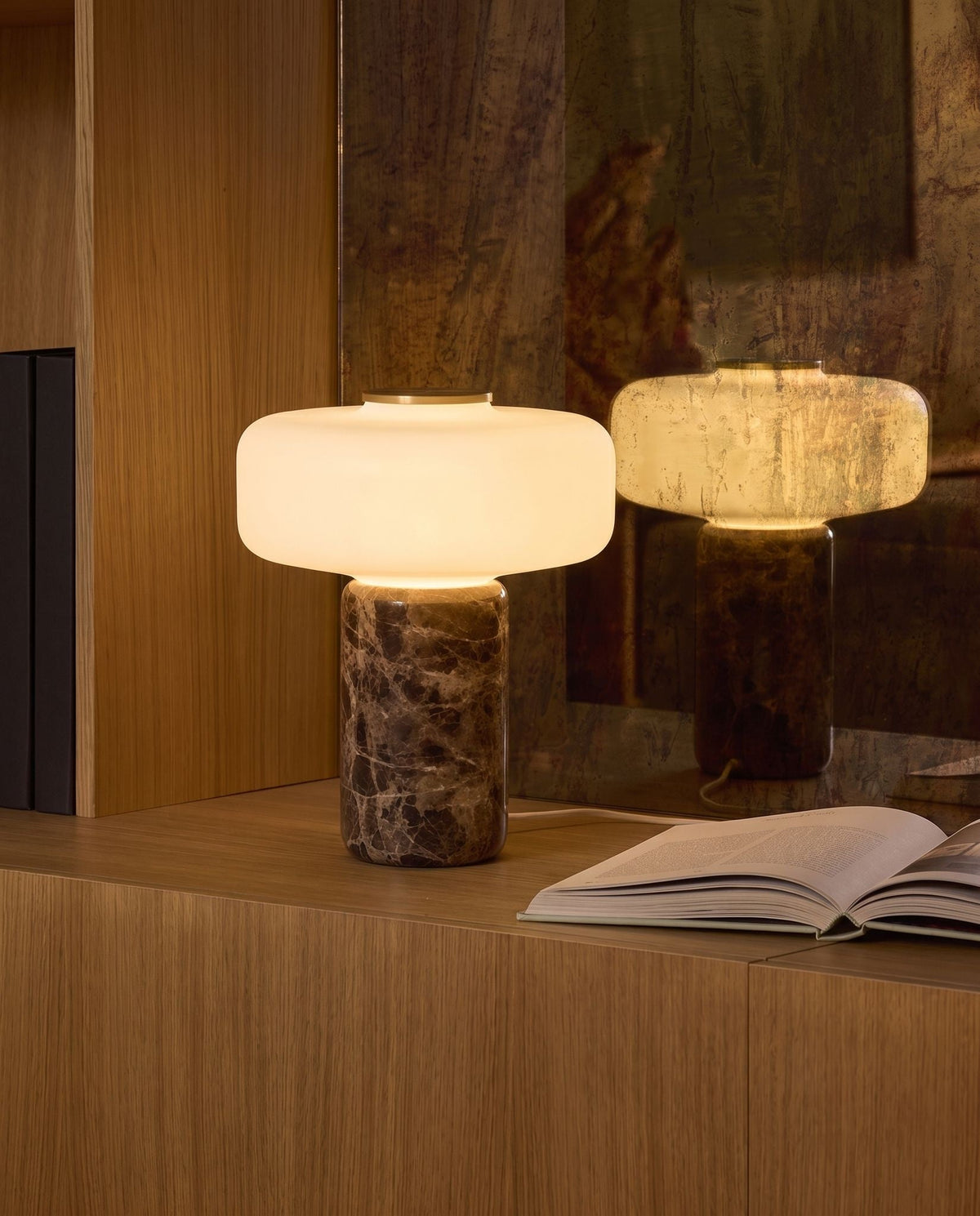 Lysa marble and glass table lamp, lit, on an oak cabinet before an antique mirror