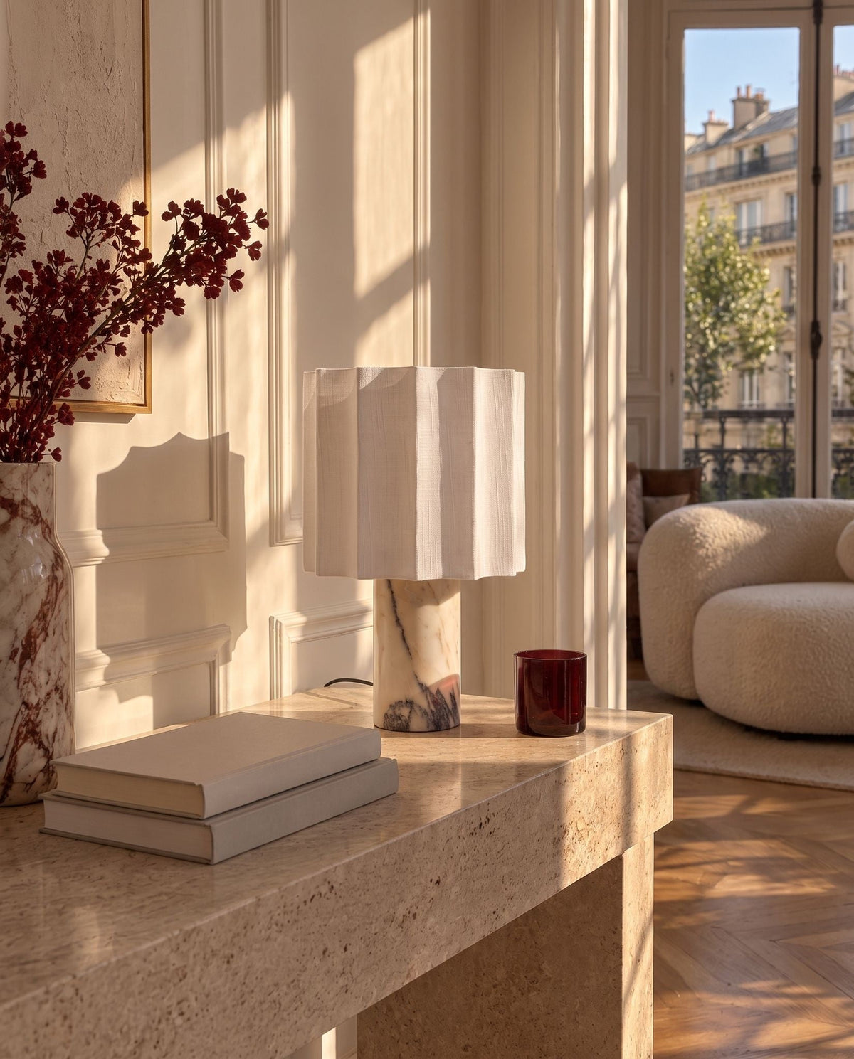 Macara marble and fabric table lamp on a travertine console in a sunlit living room with a boucle armchair