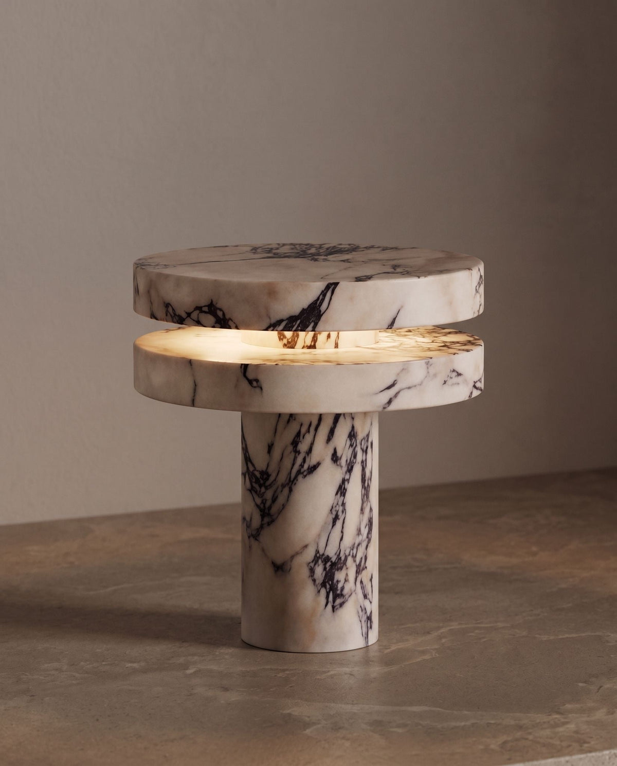 Strates marble table lamp, lit, on a stone ledge against a taupe wall