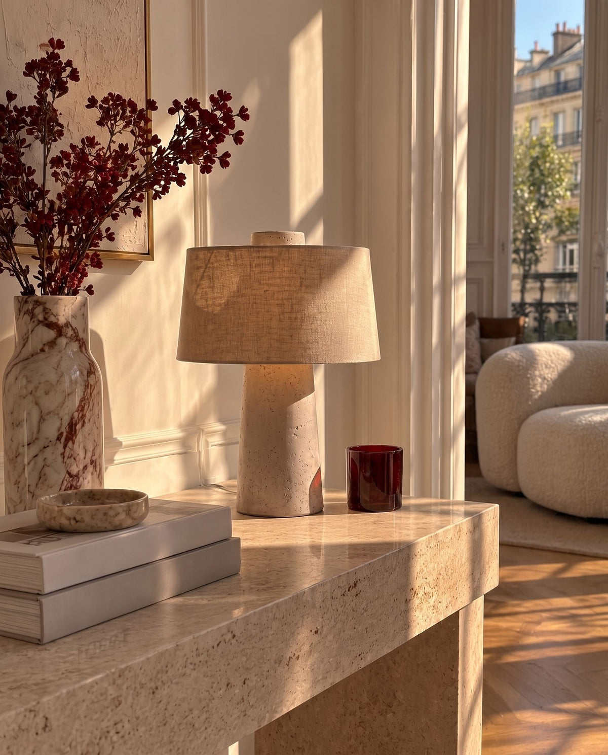 Tellur travertine and fabric table lamp on a travertine console in a sunlit living room with a boucle armchair