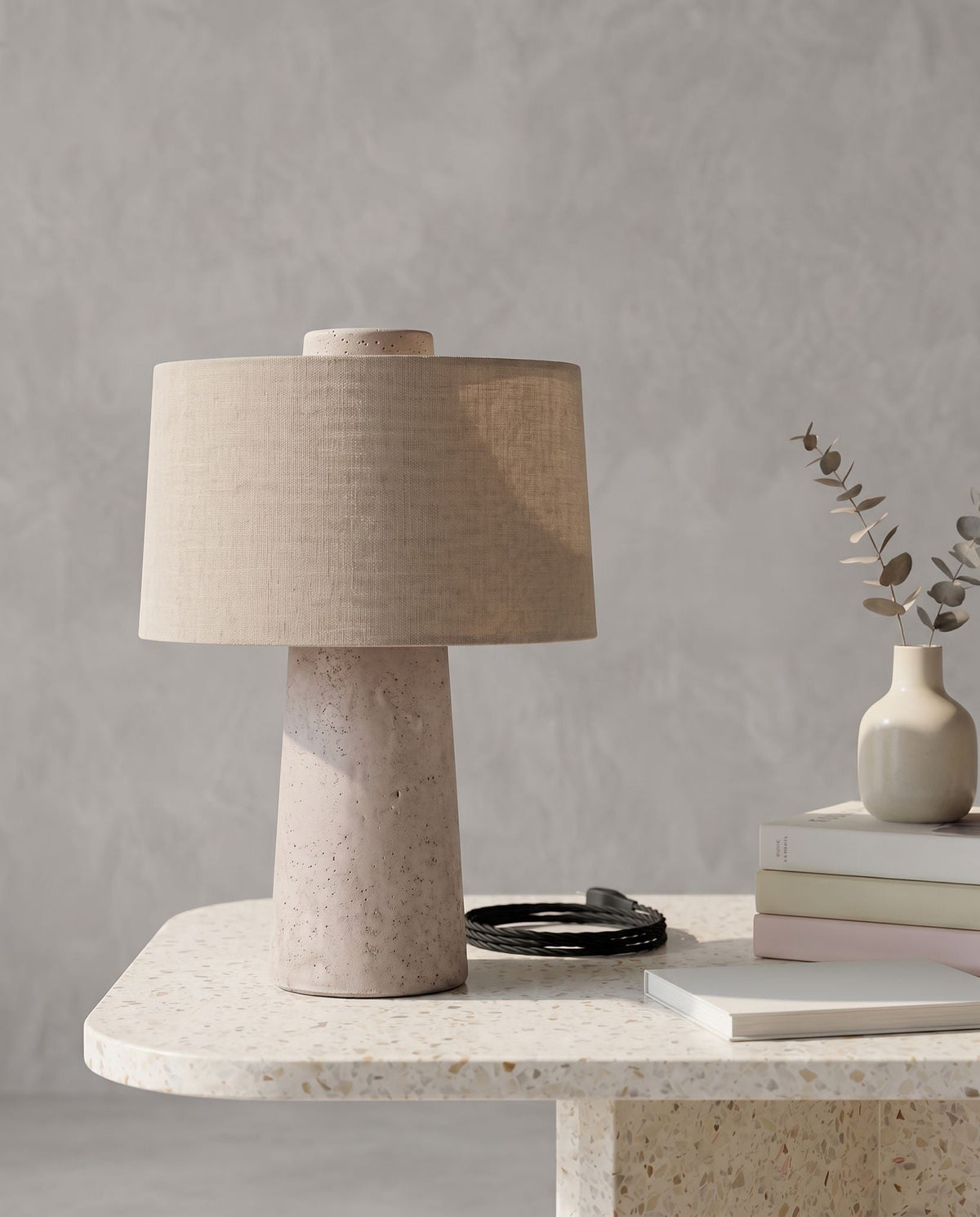 Tellur travertine and fabric table lamp on a terrazzo table, its black cord coiled beside it