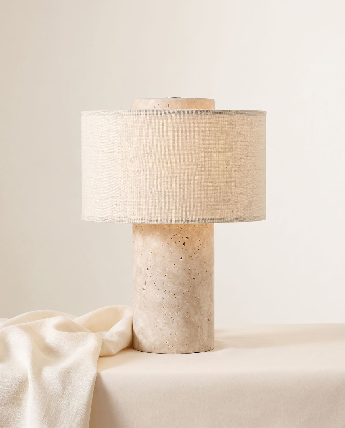Auren rechargeable stone table lamp beside draped cream fabric on off-white backdrop