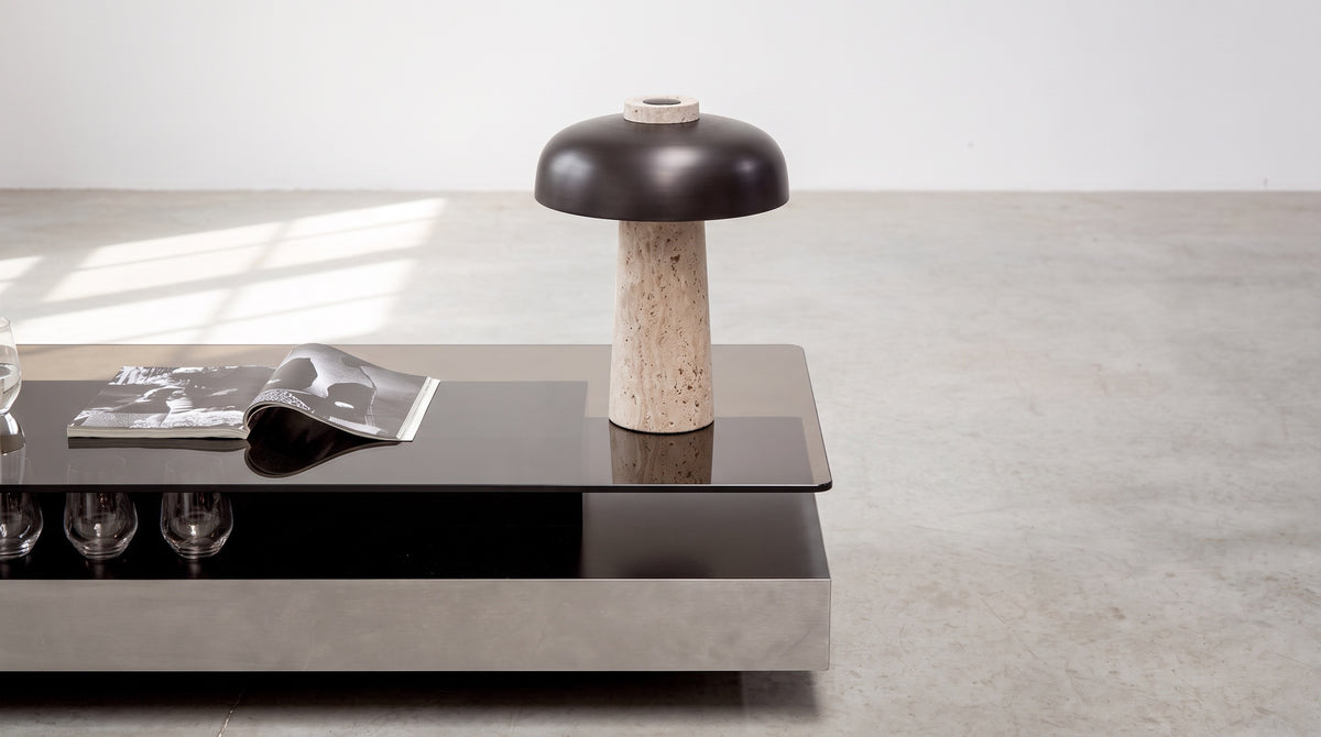 Silex rechargeable travertine table lamp on a smoked glass coffee table, concrete floor