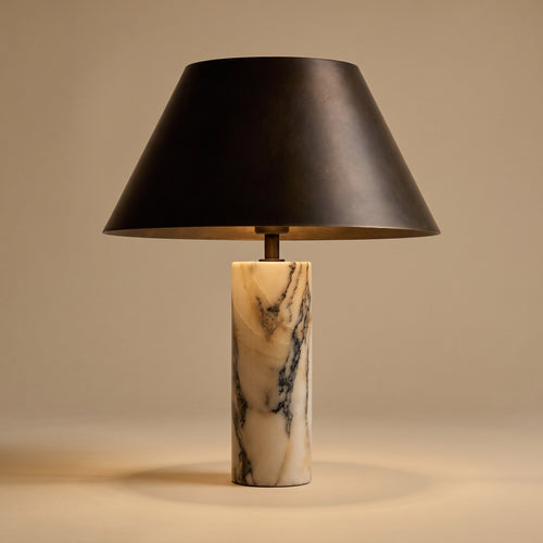 Cline Vesper marble and metal table lamp, lit, on a warm beige studio background