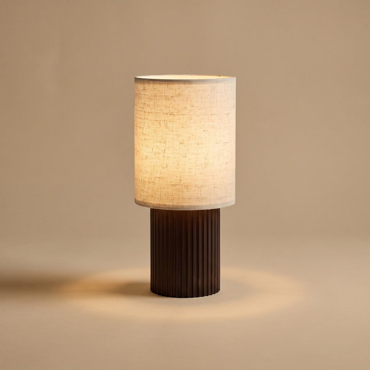 Colonne aluminum and linen table lamp, lit, on beige backdrop