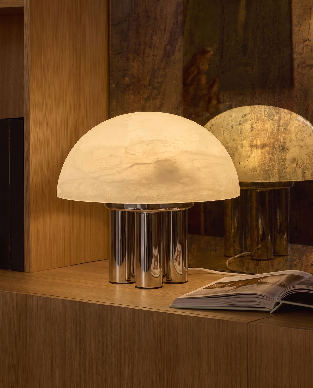 Iris dome table lamp, lit, on an oak cabinet, antique mirror behind