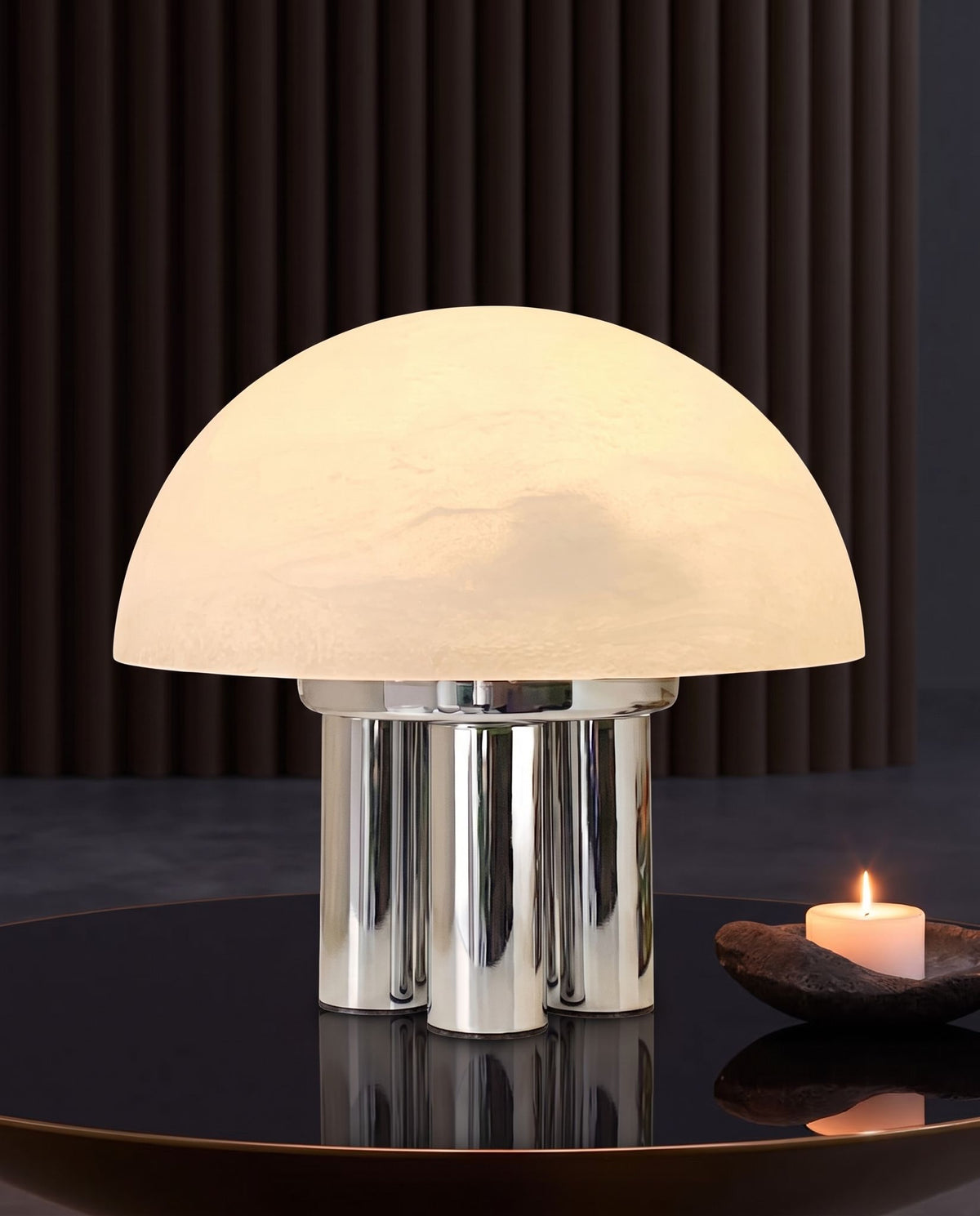 Iris dome table lamp, lit, on a black glossy table with a candle, fluted dark wall