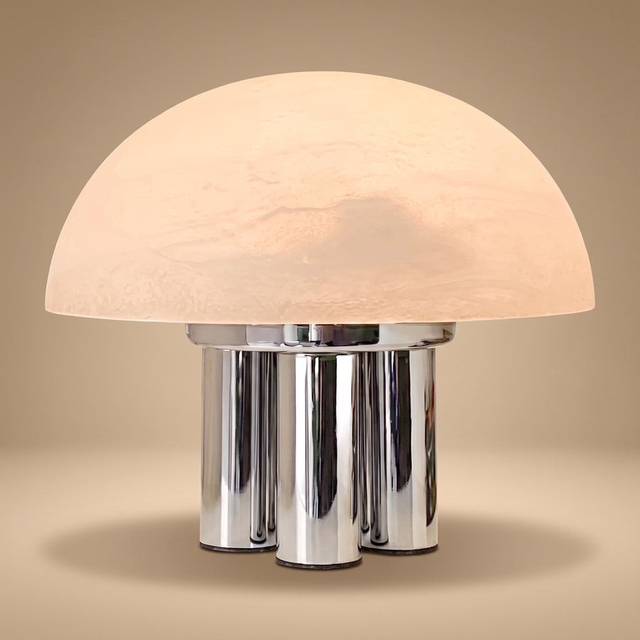 Iris dome table lamp, lit, on four chrome columns against a warm beige backdrop