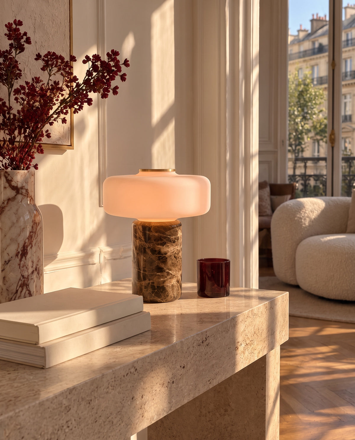 Lysa marble and glass table lamp, lit, in a sunlit Parisian living room with boucle armchair