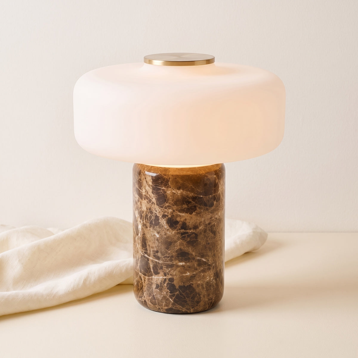 Lysa marble and glass table lamp, lit, beside draped linen