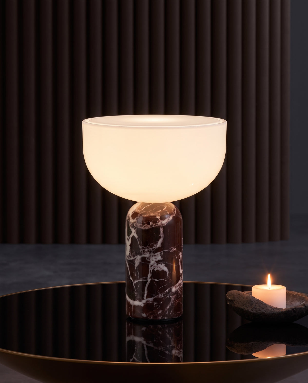 New Works marble and glass table lamp, lit, on a mirrored table before a fluted dark wall