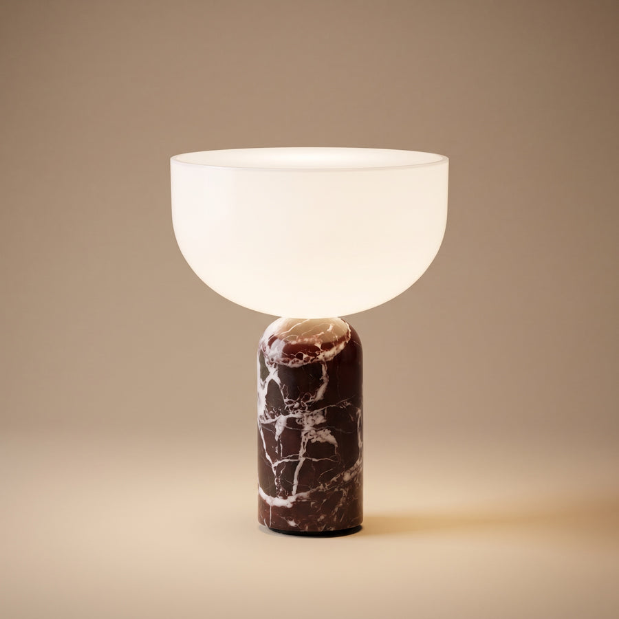 New Works marble and glass table lamp, lit, on warm sand backdrop