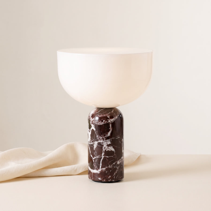 New Works marble and glass table lamp beside folded cream linen on an off-white backdrop