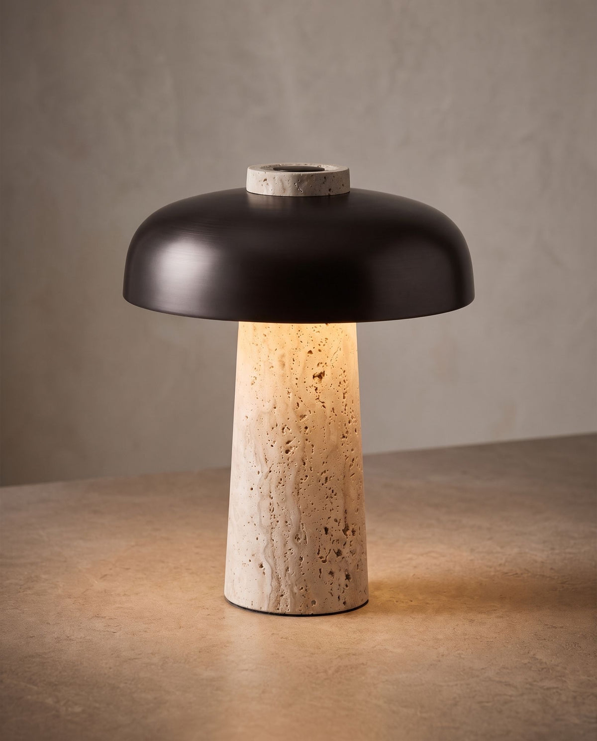 Silex rechargeable travertine table lamp, lit, against a warm plaster wall