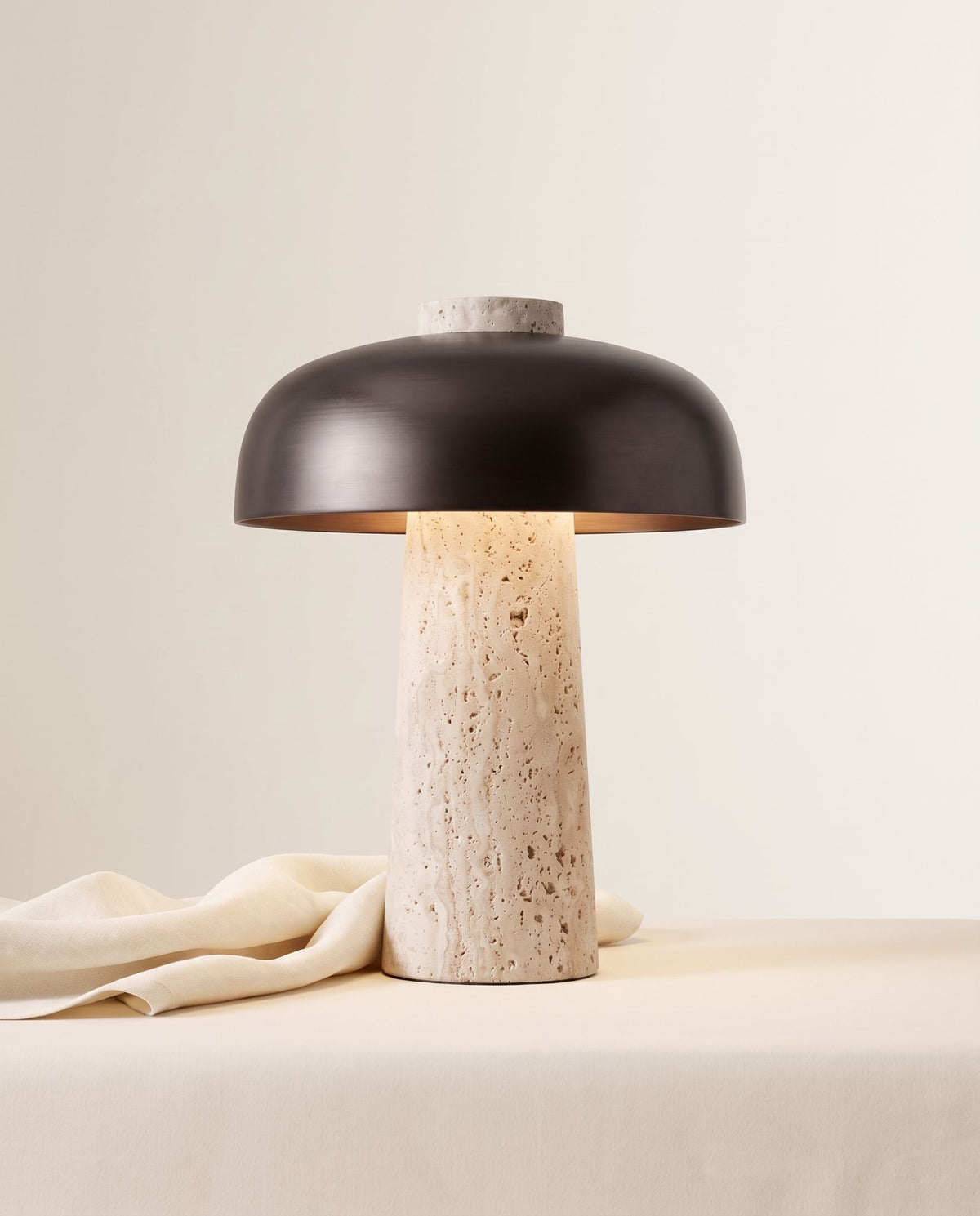 Silex rechargeable travertine table lamp, lit, on a cream draped table against an off-white backdrop