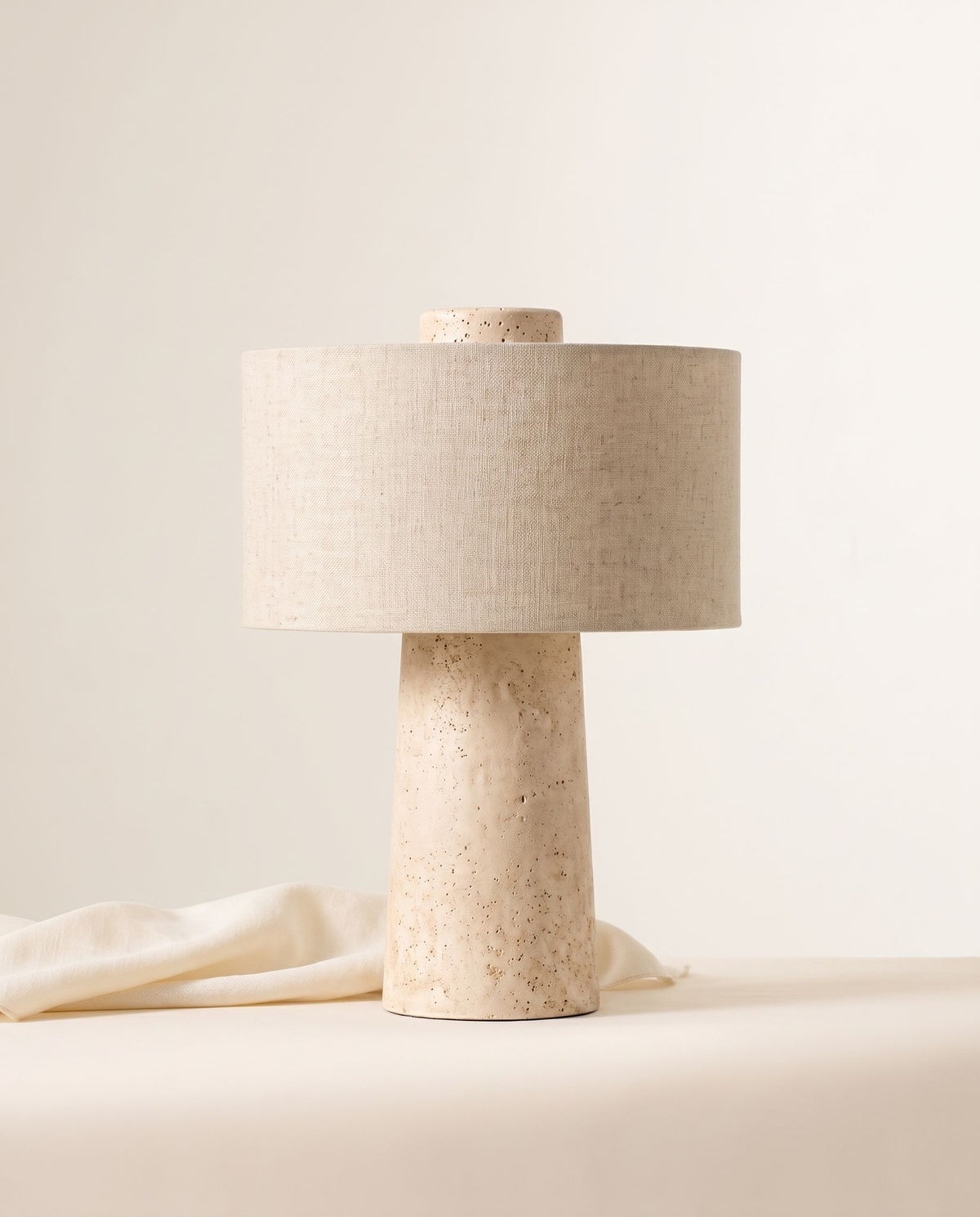Tellur travertine and fabric table lamp on a cream backdrop, linen cloth