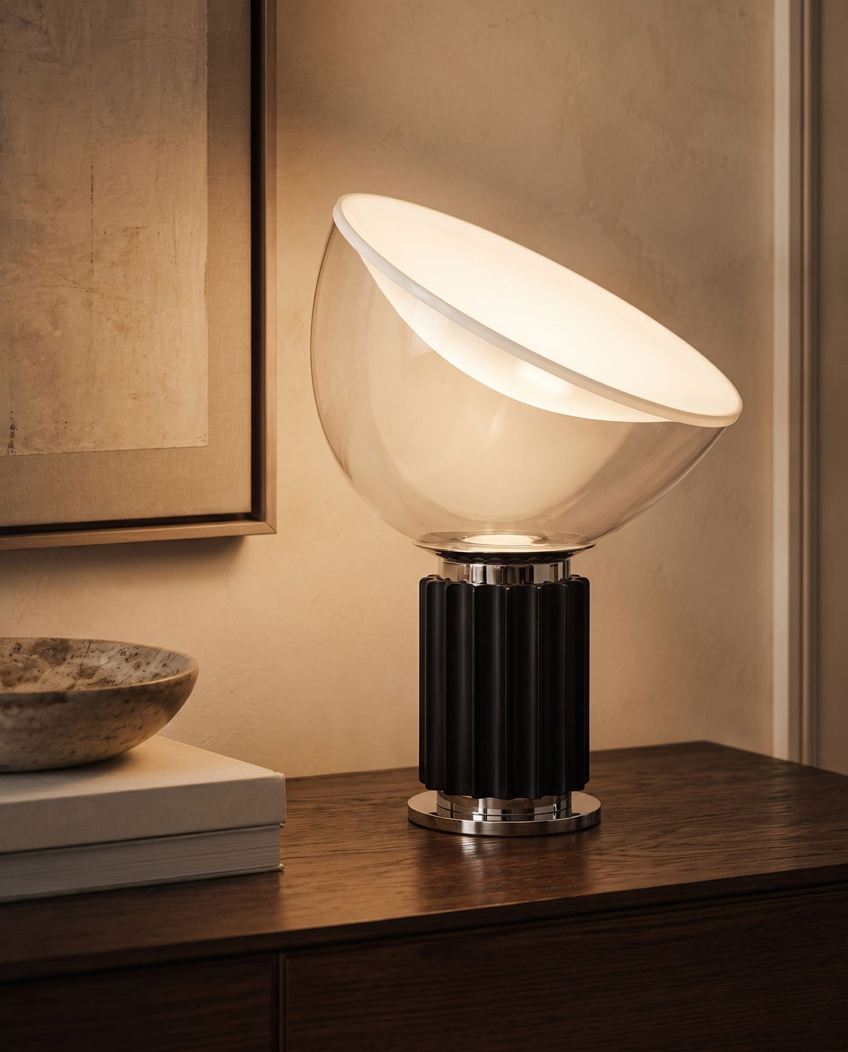 Zenith glass and metal table lamp, lit, on dark wood dresser beside framed art